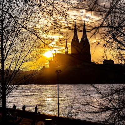 Die Silhouette des Kölner Doms ist im Sonnenuntergang von der gegenüberliegenden Seite des Rheins zu sehen.