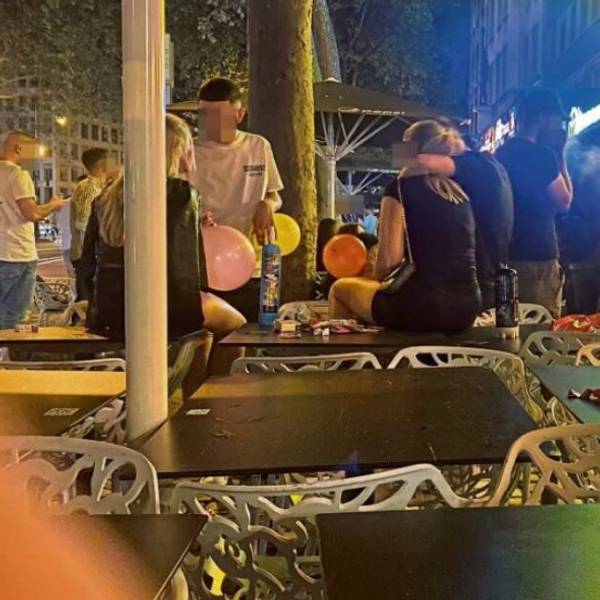 Junge Männer und Frauen sitzen mit Luftballons voller Lachgas auf Tischen an den Kölner Ringen.