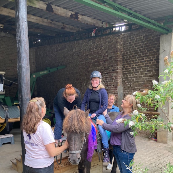 Die Schülerin sitzt auf einem Pferd, mehrere Frauen stehen drumherum.