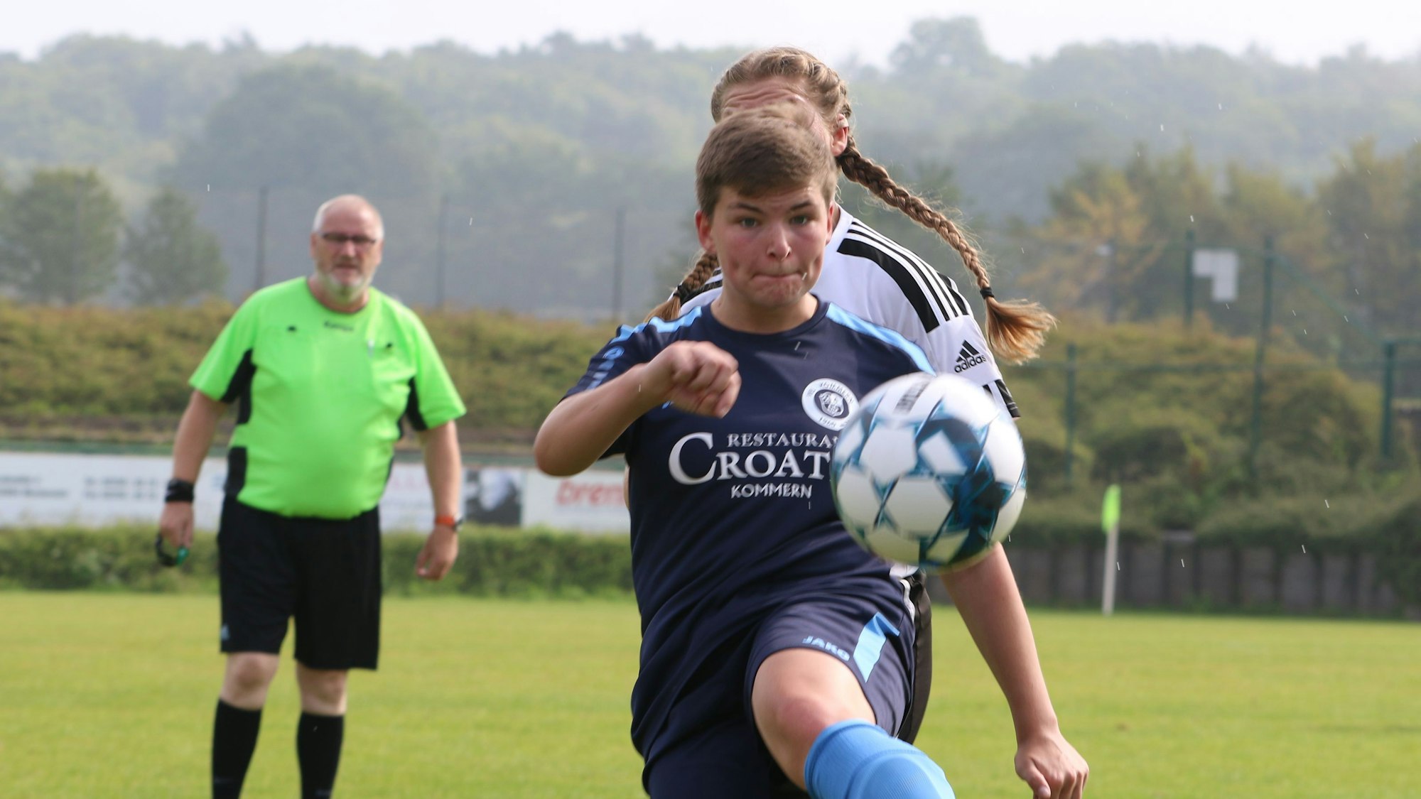 Kommerns Spielerin Laurie Simon schaut auf den Ball. Von ihrer Gegenspielerin im Hintergrund sind Zöpfe zu sehen.