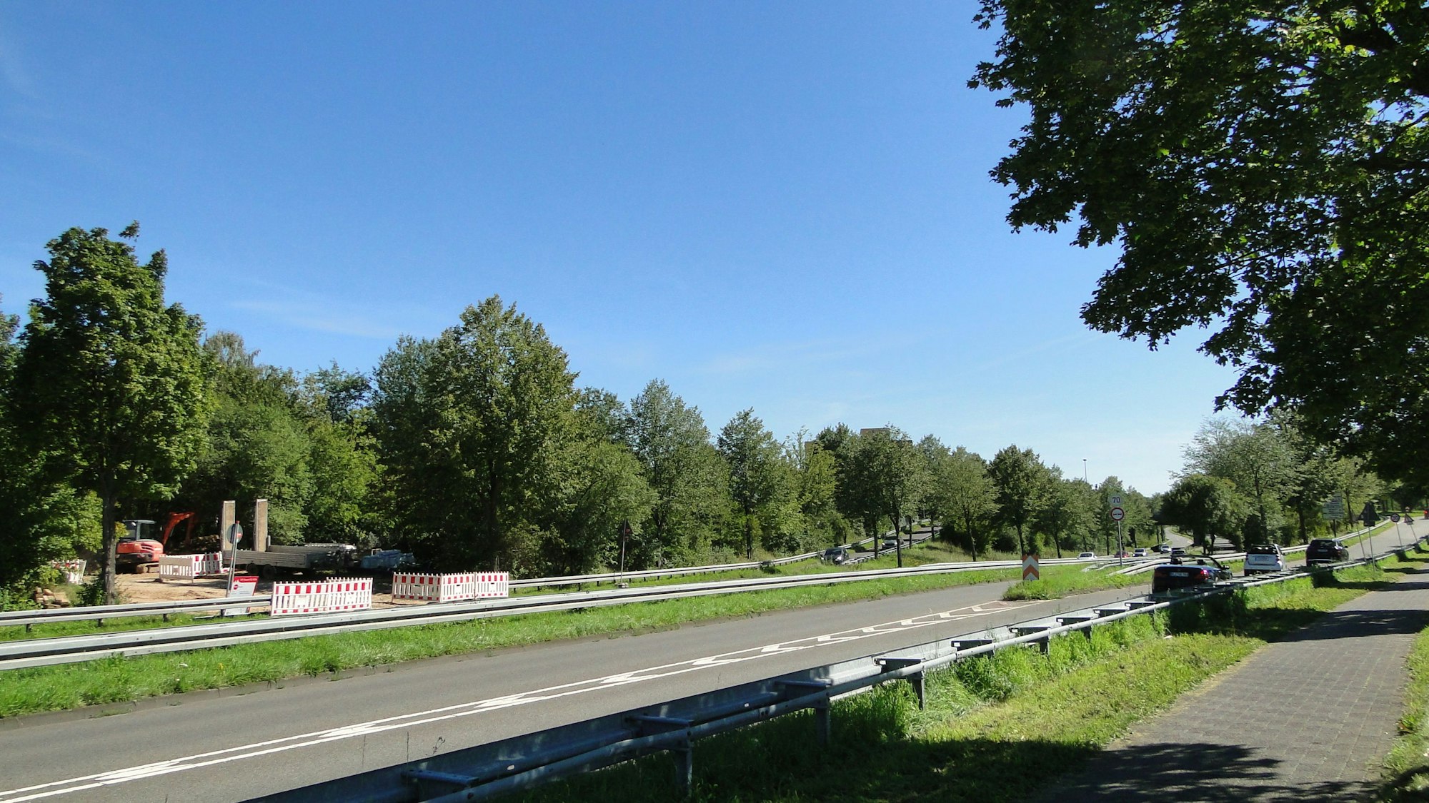Eine mehrspurige Straße mit Bäumen links und rechts ist zu sehen.