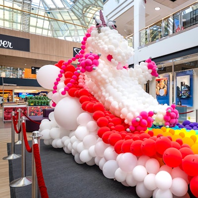 Ein Einhorn mit Regenbogen aus Luftballons steht im Erdgeschoss eiens großen Einkaufszentrums.