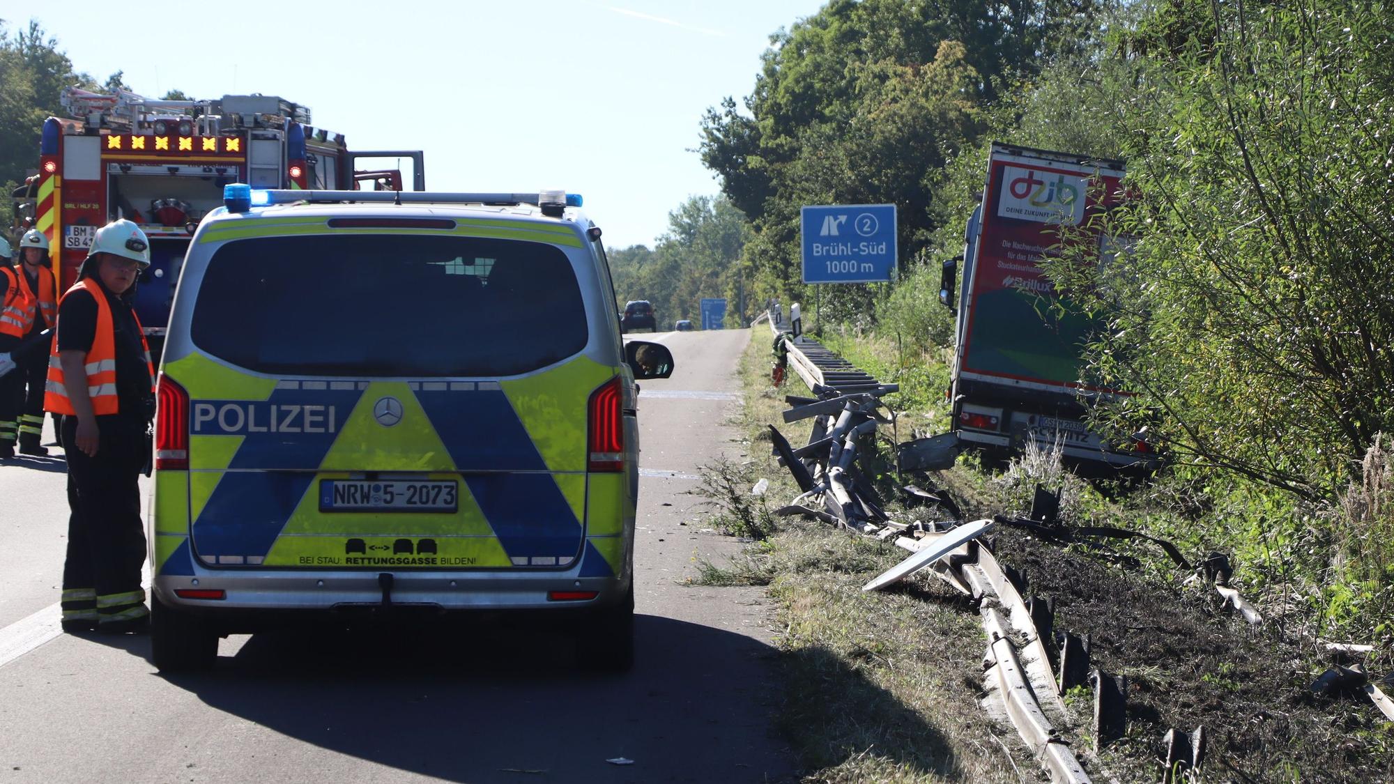 Zu sehen ist ein Polizeiwagen sowie eine demolierte Leitplanke. Im Hintergrund steht der verunglückte Laster.