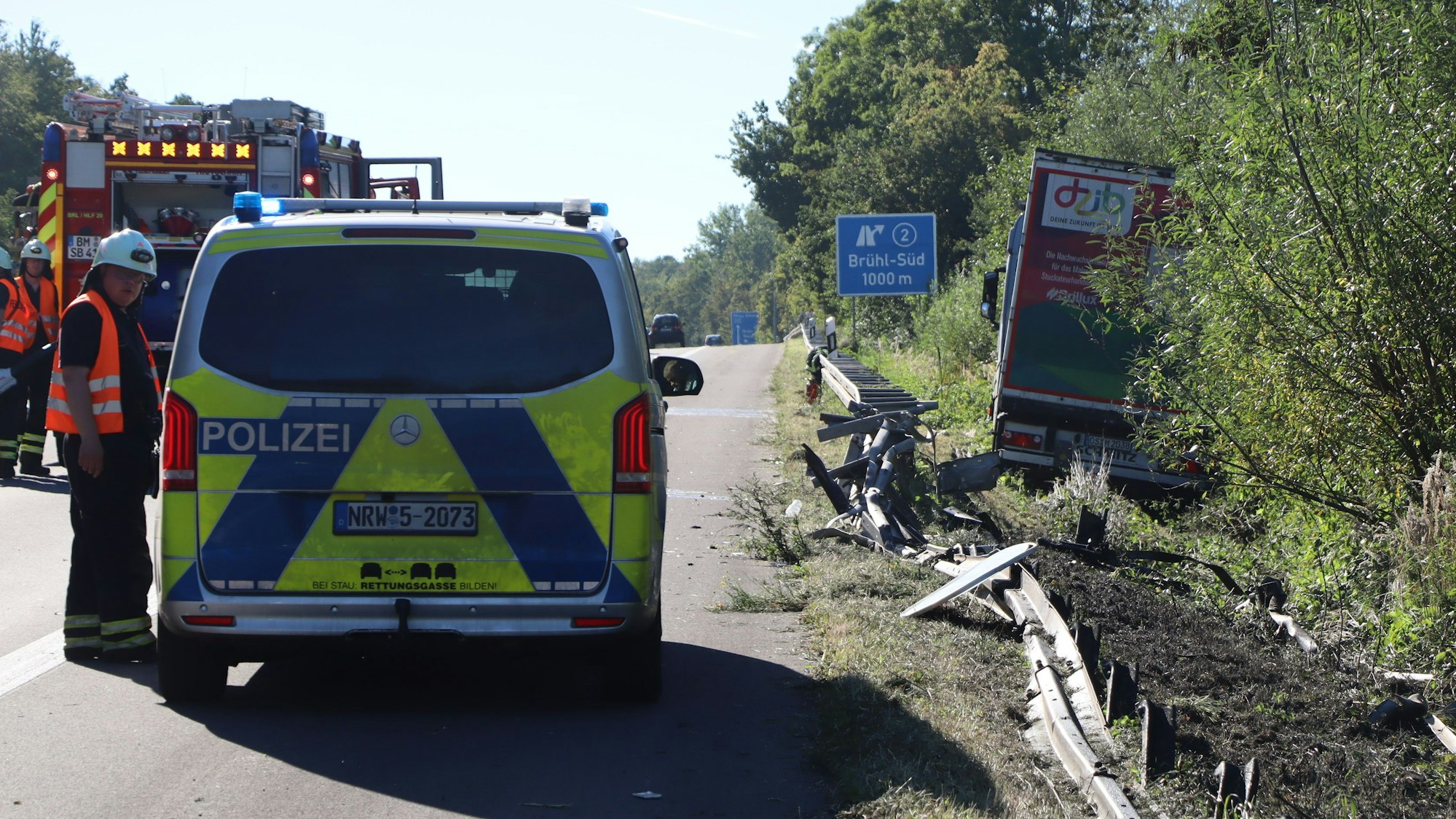 Zu sehen ist ein Polizeiwagen sowie eine demolierte Leitplanke. Im Hintergrund steht der verunglückte Laster.