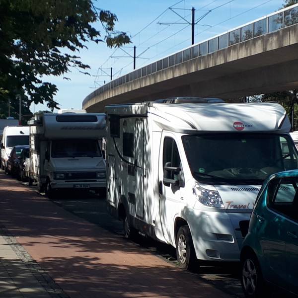 Mehrere Wohnmobile parken hintereinander an einer Straße.