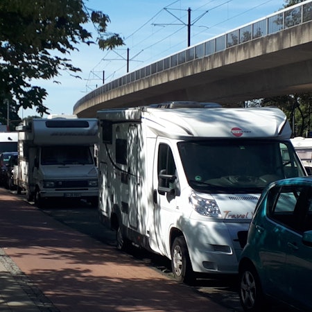 Mehrere Wohnmobile parken hintereinander an einer Straße.