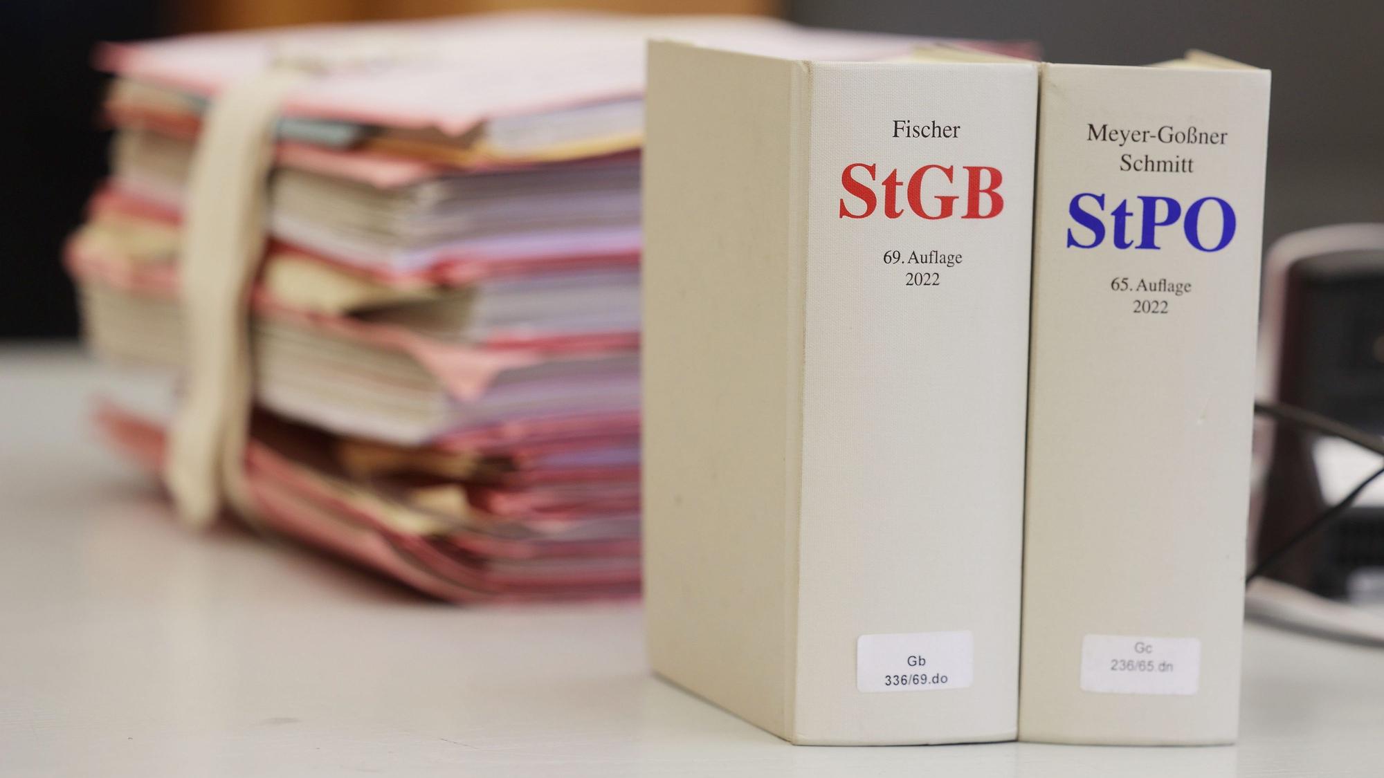 Gerichtsakten und Bücher zu Strafgesetzbuch und Strafprozessordnung liegen bzw. stehen liegen auf einem Tisch in einem Gerichtssaal.