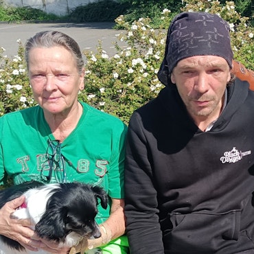 In der Mitte sitzt der Obdachlose Andreas Wüntenberg. Neben ihm sitzen zwei Frauen.