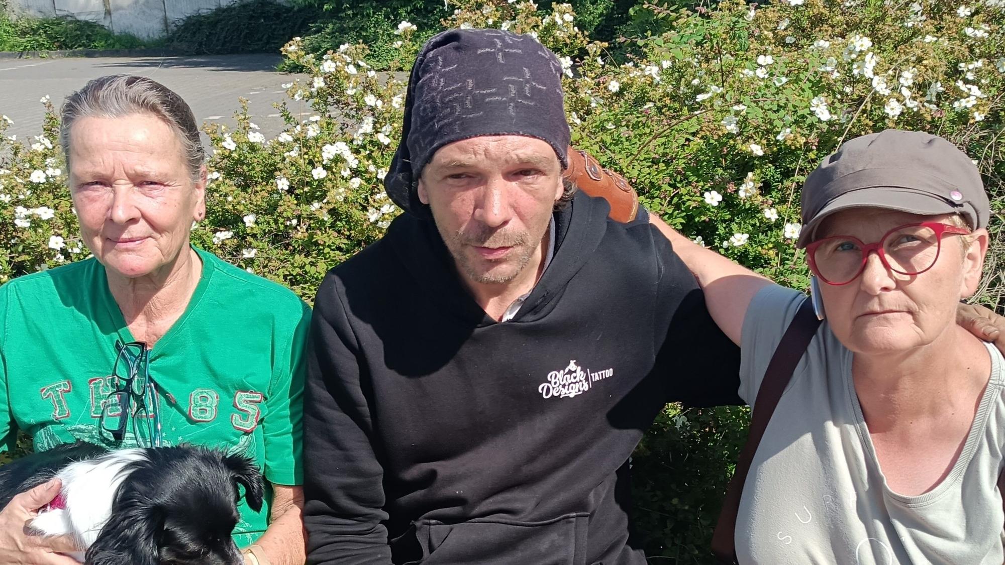 In der Mitte sitzt der Obdachlose Andreas Wüntenberg. Neben ihm sitzen zwei Frauen.