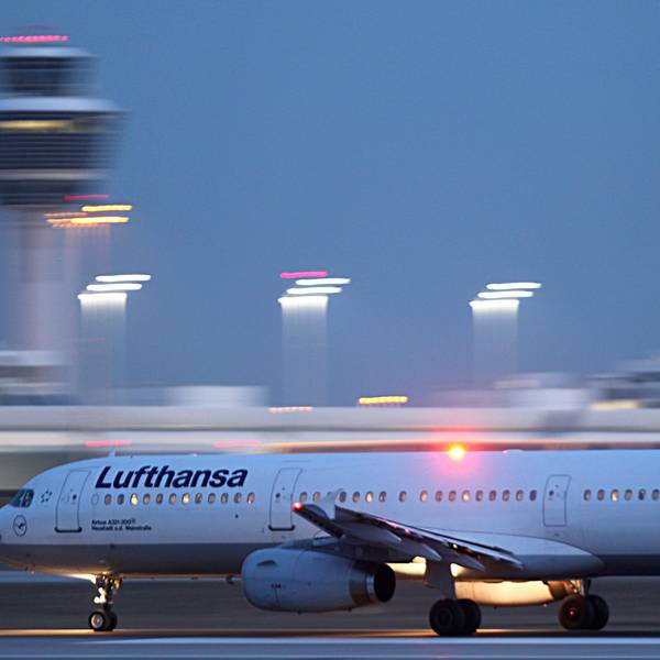 Ein Airbus A321 der deutschen Fluggesellschaft Lufthansa startet auf einem Flughafen. Im Hintergrund sind verschwommen Scheinwerfer der Startbahn und der Flughafentower zu sehen. (Symbolbild)