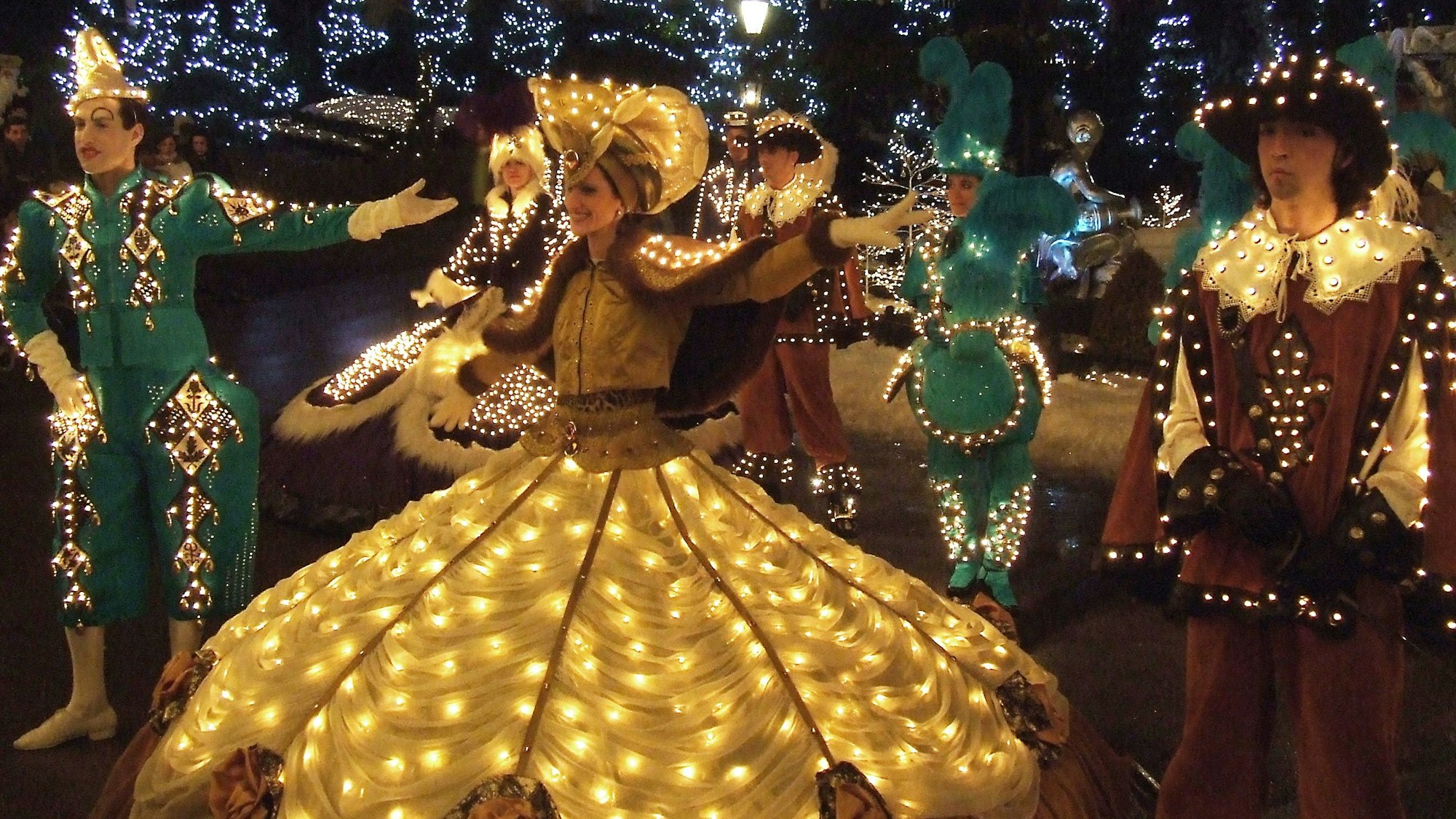 Menschen in gelber, grüner und brauner Kleidung in mittelalterlich-anmutedem Stil leuchten in der Nacht, winzige LED-Lampen sind in den Kleidern befestigt.