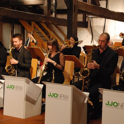 Mehrere Frauen und Männer sitzen an Notenpulten und spielen Instrumente.