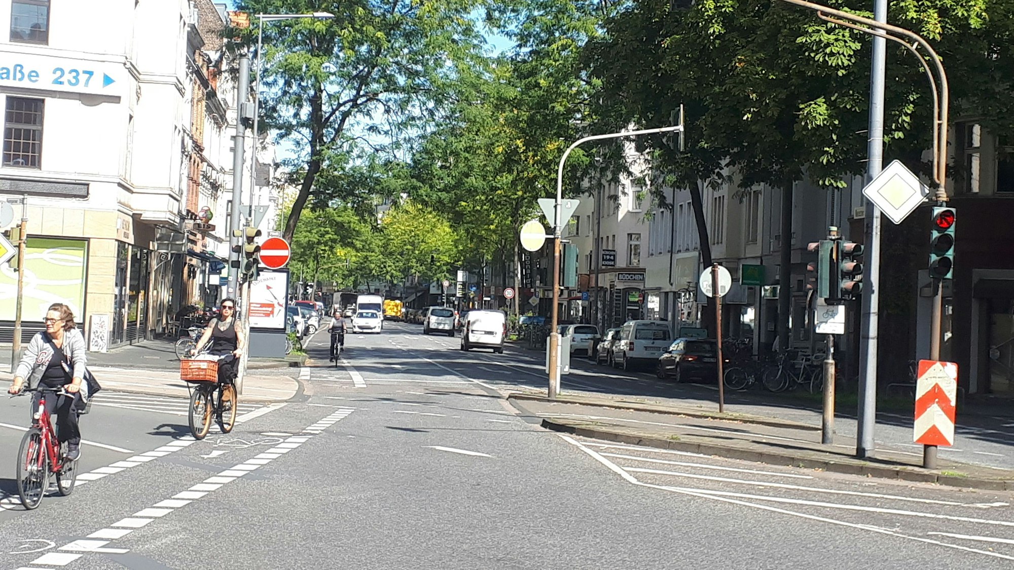 Die Kreuzung Neusser/Kempener/ Auerstraße ist zu sehen. Drei Straßen treffen aufeinander, Radfahrerinnen radeln über die Kreuzung.
