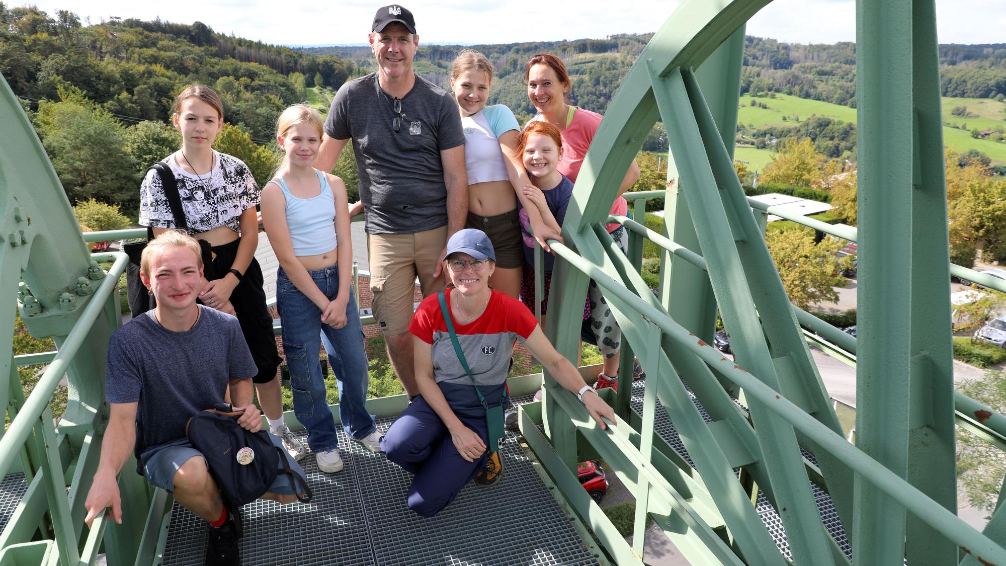 Eine Gruppe von Erwachsenen und Kindern steht neben Seilscheiben eines Fördergerüst auf dessen oberster Plattform.