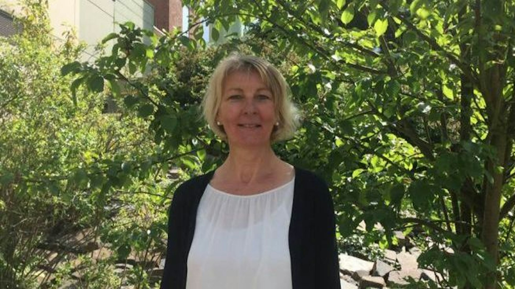 Frau Naderer ist im Halbporträt zu sehen, sie steht vor einem sonnendurchfluteten Baum.