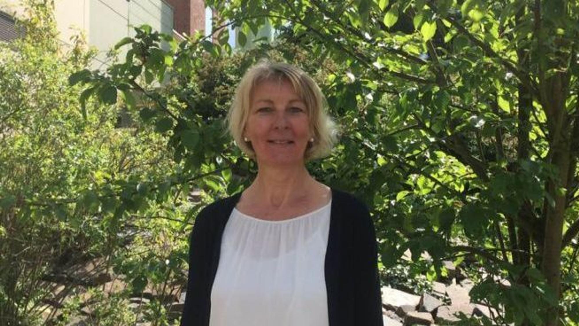 Frau Naderer ist im Halbporträt zu sehen, sie steht vor einem sonnendurchfluteten Baum.