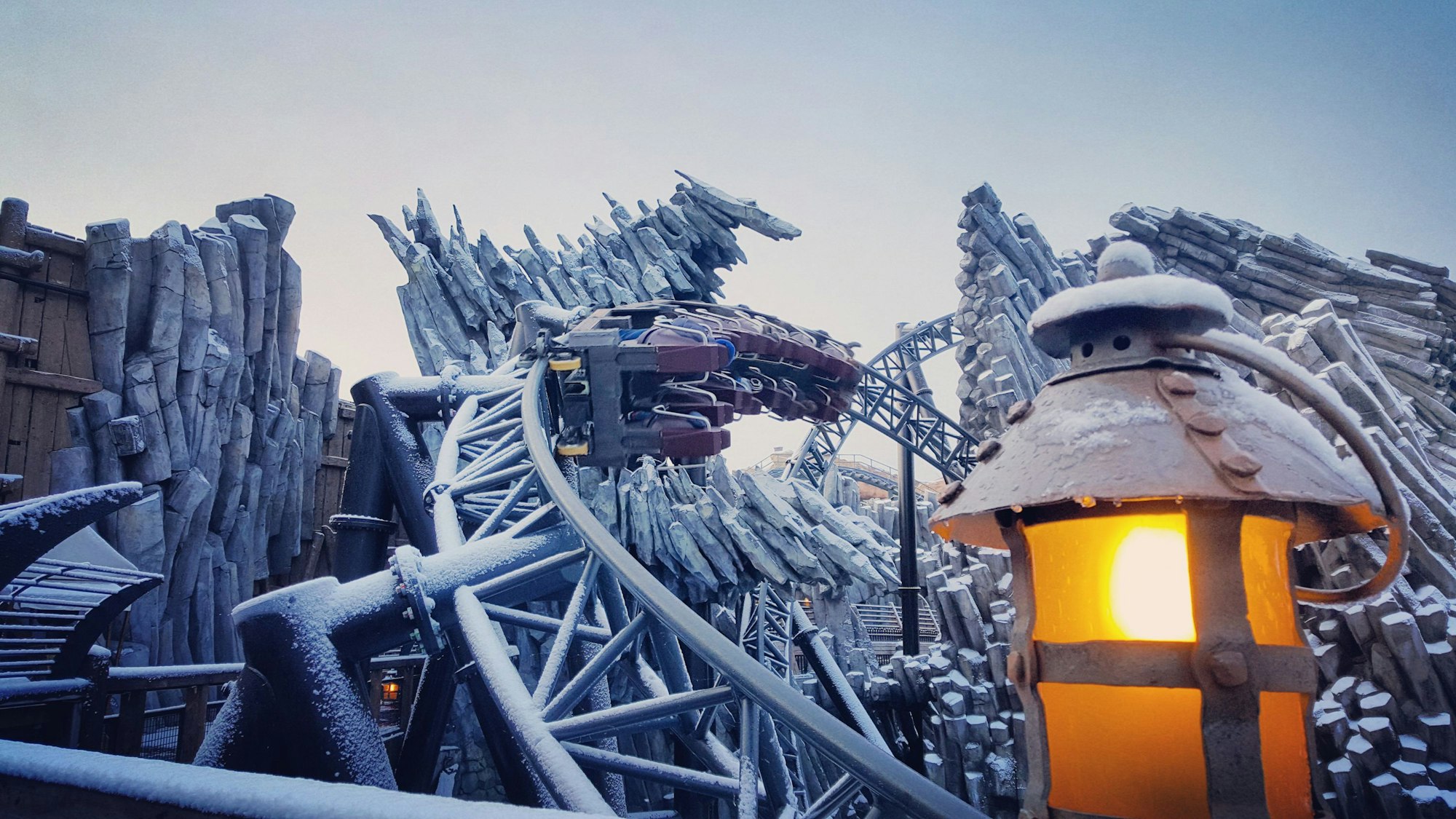 Auf vereisten Schienen fährt die Achterbahn „Taron“ im Phantasialand. Im Vordergrund brennt eine Laterne, im Hintergrund sind frostige Steinformationen zu sehen.