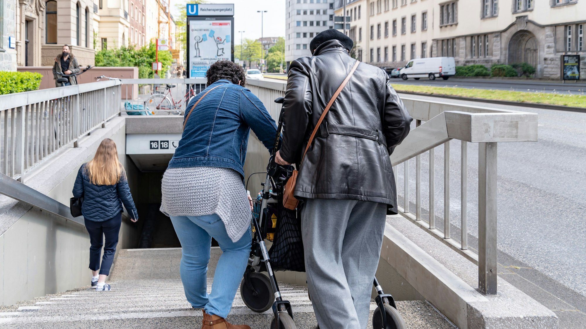 Eine Frau hilft ihrer kranken Freundin wegen fehlendem Aufzug dabei, die Treppe hinabzusteigen.