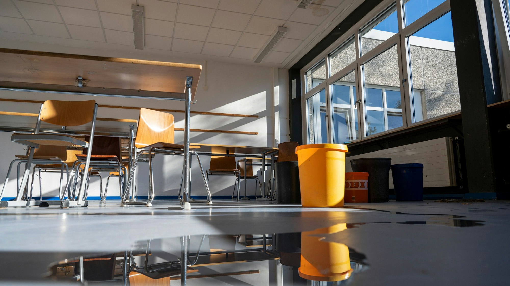 Ein Eimer steht in einer leeren Klasse, davor eine Pfütze.