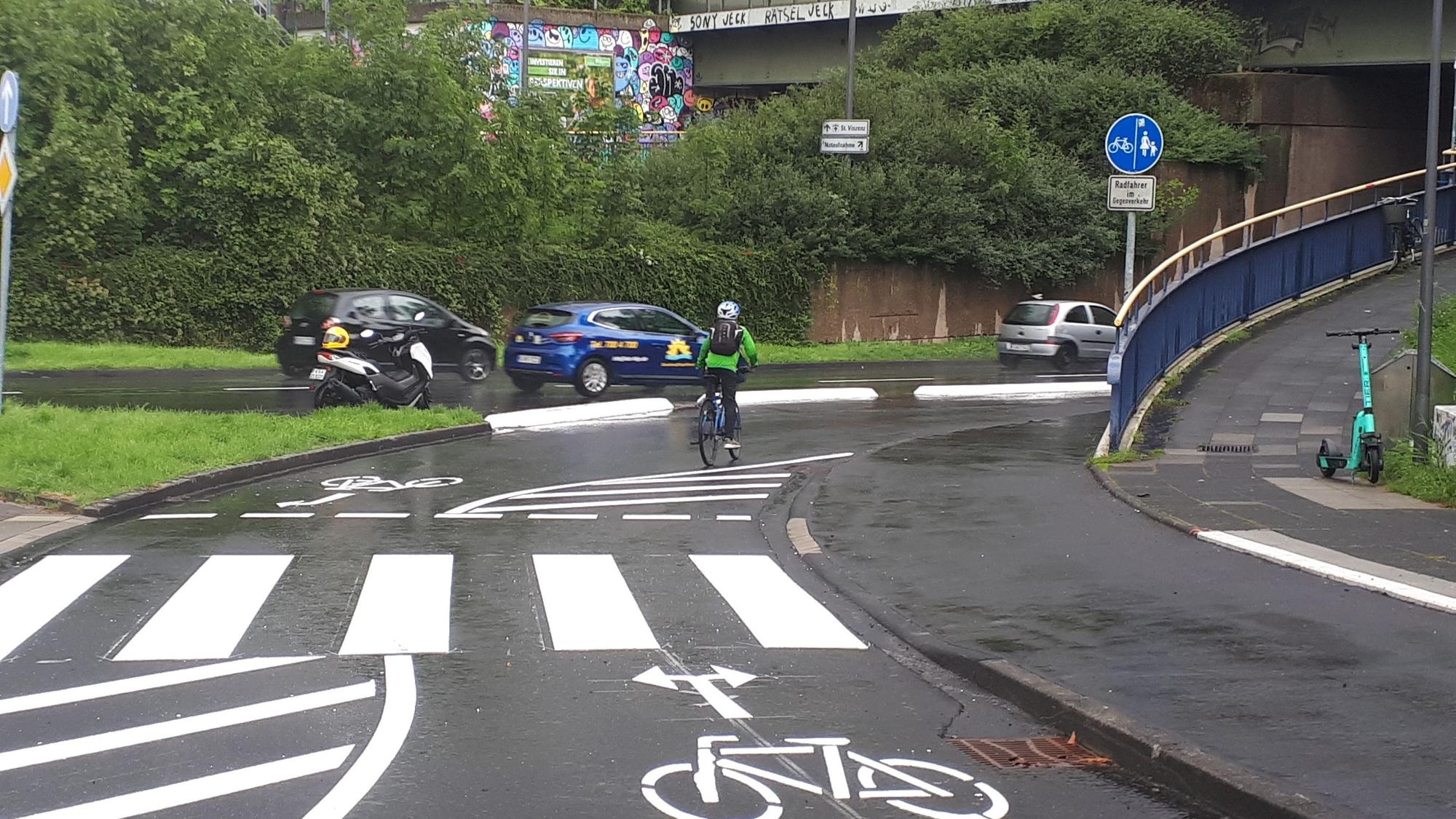 Ein Radfahrer fährt auf der einer Radspur an einer zweispurigen Straße. Es sind Fahrradpiktogramme mit Richtungspfeile und ein Zebrastreifen aufgemalt.