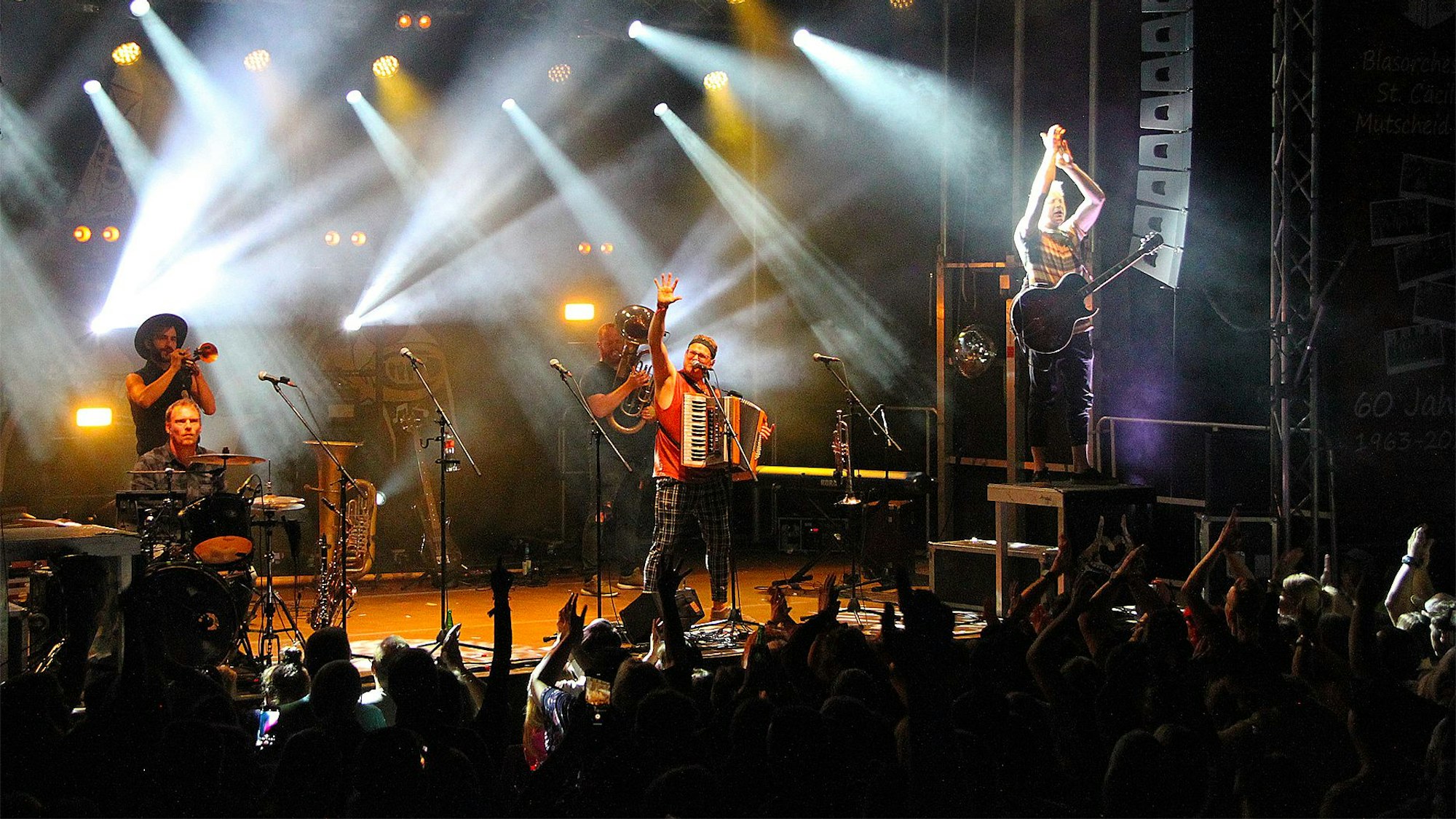 Die Band Fäaschtbänkler steht bei ihrem Konzert in Mutscheid auf der Bühne. Davor ist im Dunkeln eine klatschende Menschenmenge zu erahnen.