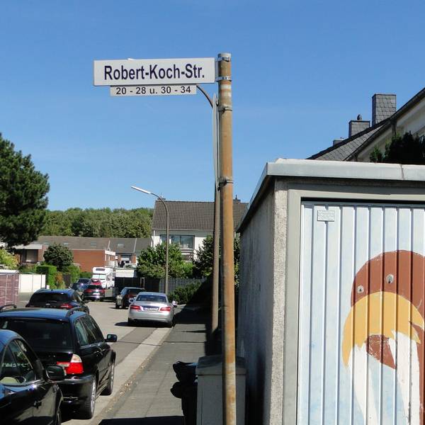 Ein Straßenschild mit der Aufschrift „Robert-Koch-Str.“ steht an einer Straßenecke.