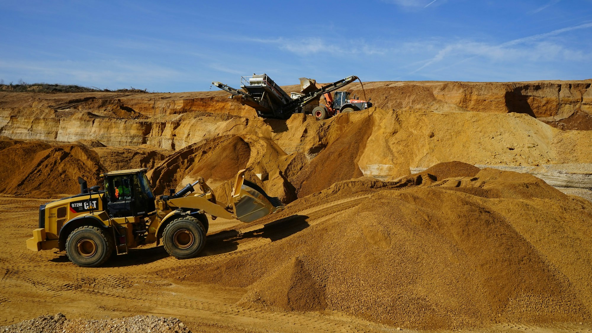 Das Bild zeigt einen Radlader und ein Förderband im Tagebau.