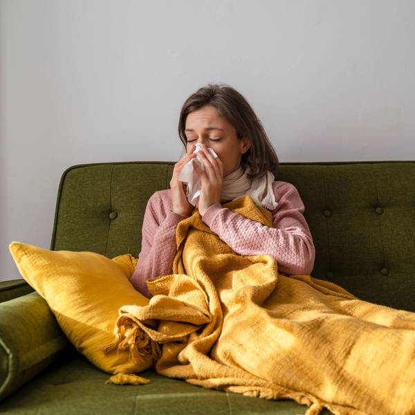 Frau sitzt auf dem Sofa und putzt sich die Nase.