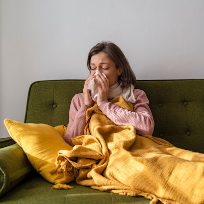 Frau sitzt auf dem Sofa und putzt sich die Nase.