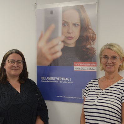 Die Leiterin der Verbraucherberatungsstelle Euskirchen, Monika Schiffer (l.), und Kriminalhauptkommissarin Eva Winkel stehen vor einem Plakat mit der Aufschrift „Bei Anruf Vertrag? Ungewollte Werbeanrufe – Wir helfen weiter!“
