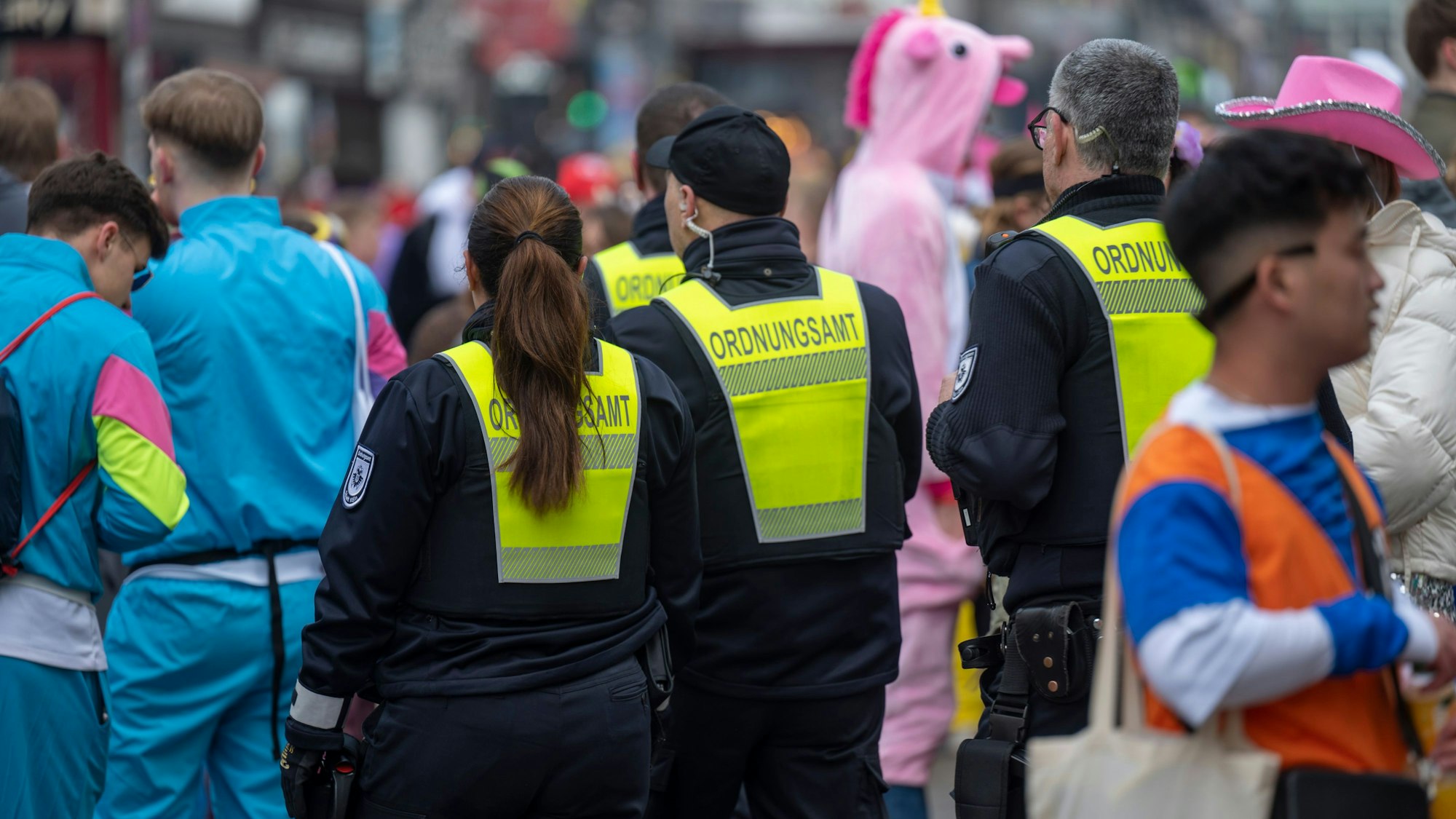 Mitarbeiter des Kölner Ordnungsamts neben Feiernden im Kwartier Latäng an Weiberfastnacht.