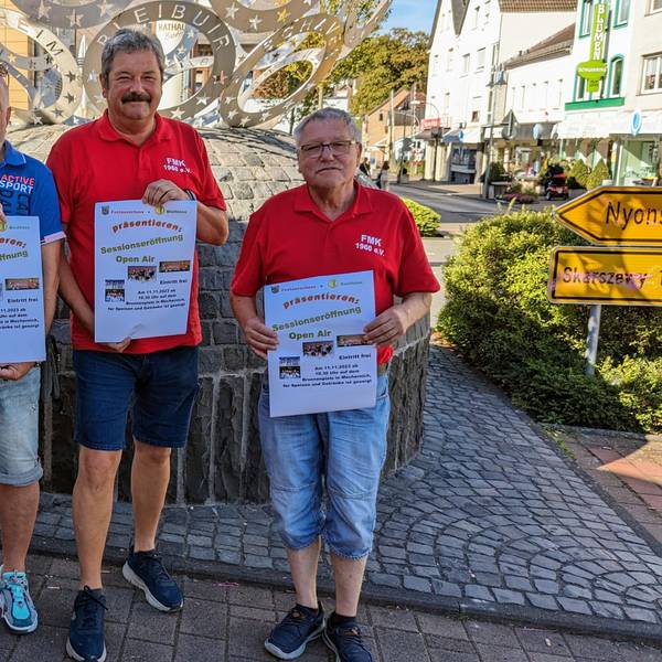 Vertreter der beiden Mechernicher Karnevalsvereine stehen in Sommerkleidung zusammen, drei Männer halten Plakate in der Hand.