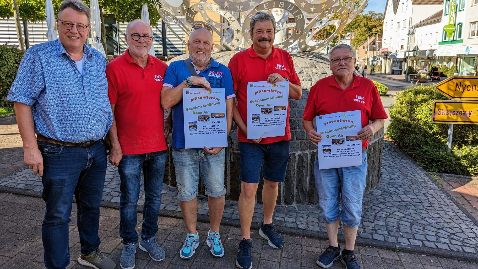 Vertreter der beiden Mechernicher Karnevalsvereine stehen in Sommerkleidung zusammen, drei Männer halten Plakate in der Hand.