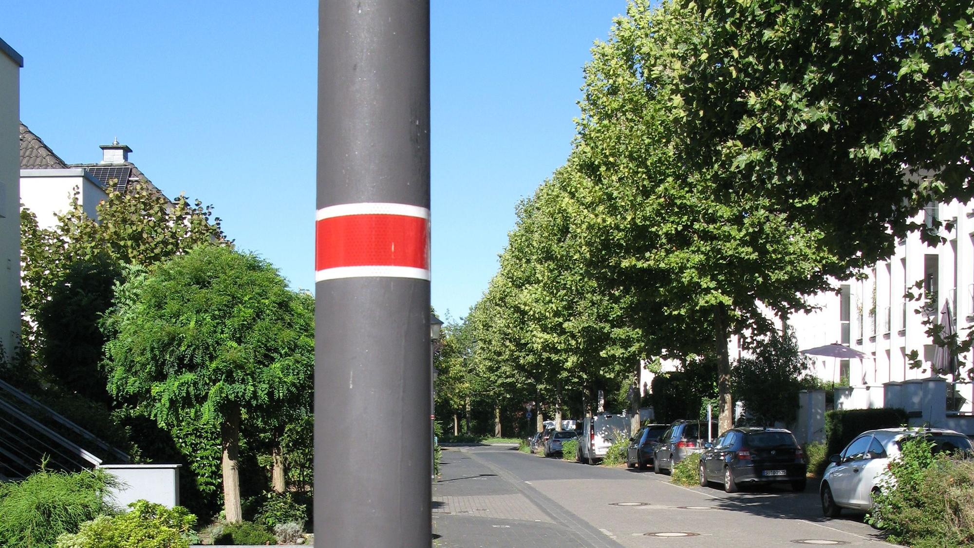 Am Mast einer Straßenlaterne ist eine rote Banderole angebracht, was bedeutet, dass diese Lampe nicht die ganze Nacht brennt.