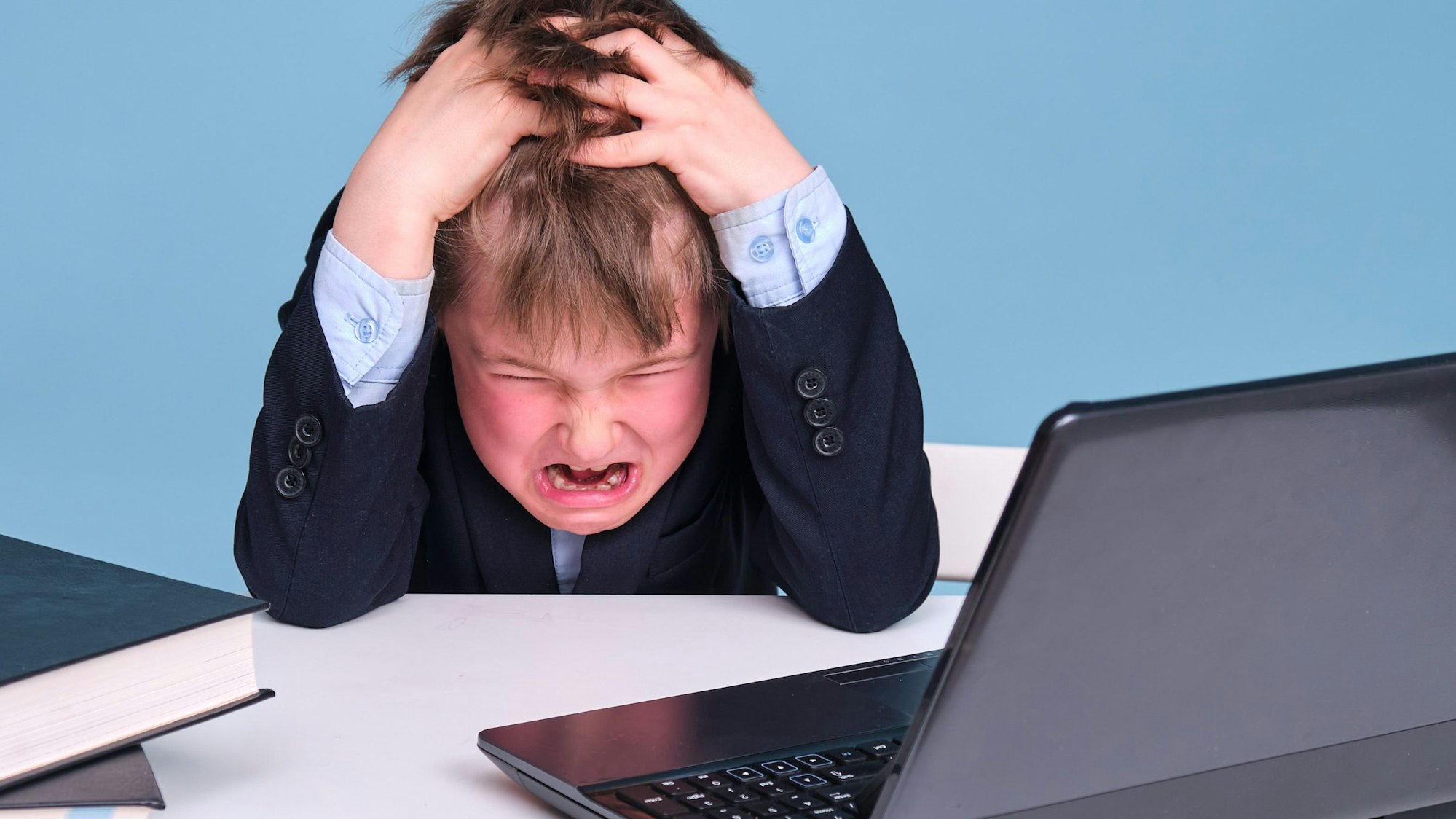 Ein kleiner Junge mit dunkelblauem Anzug sitzt wütend vor dem Computer.