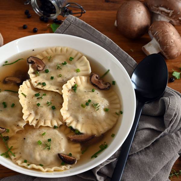 In einem Suppenteller schwimmen Ravioli und Pilze in einer Flüssigkeit.