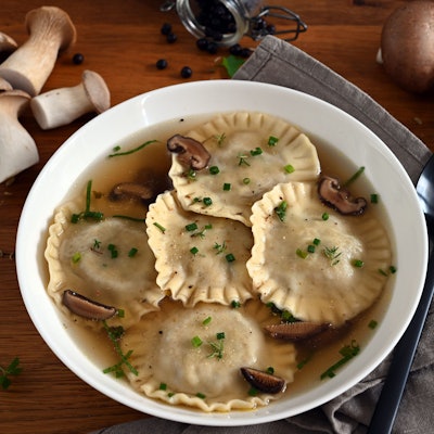 In einem Suppenteller schwimmen Ravioli und Pilze in einer Flüssigkeit.