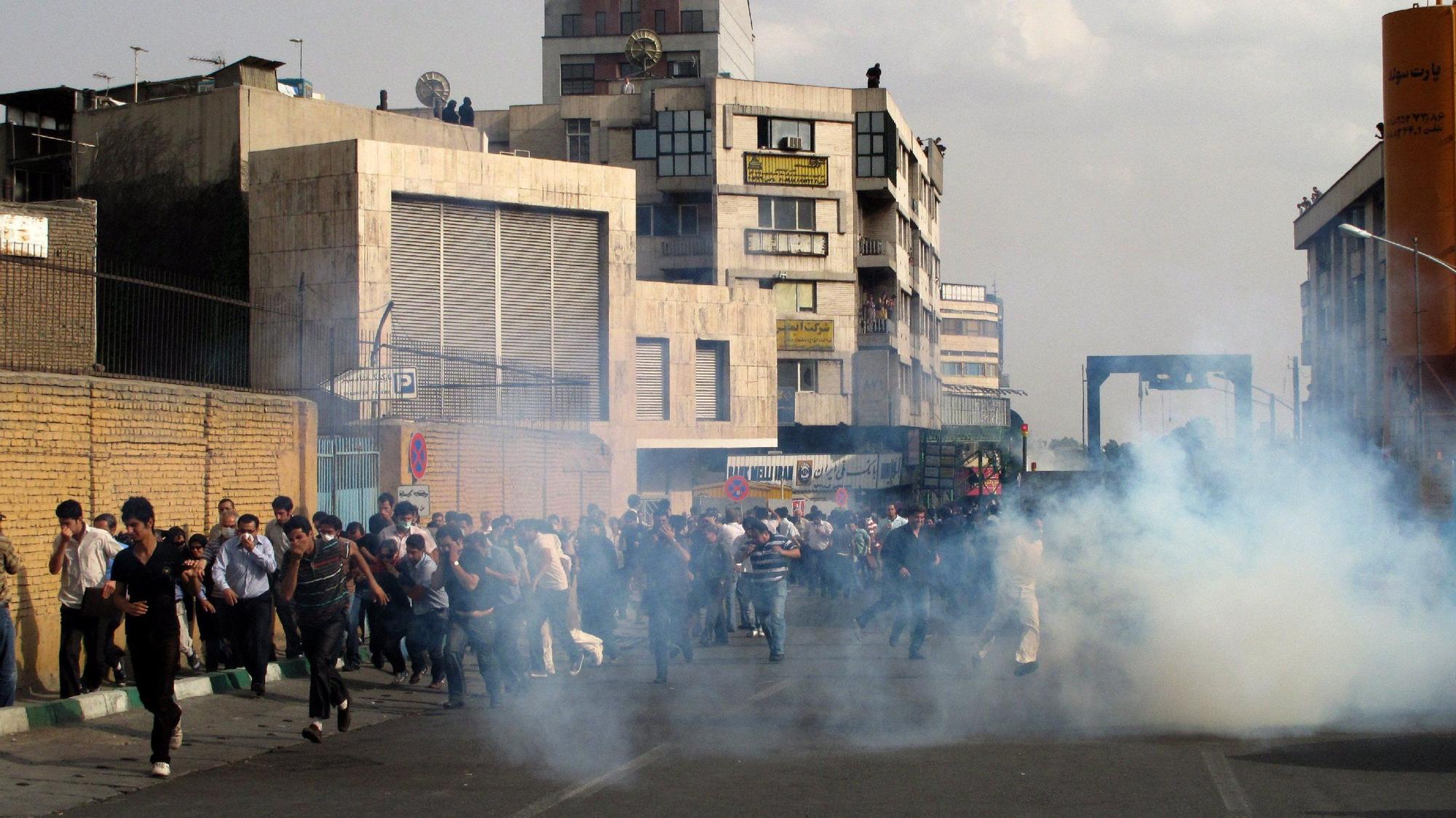 Menschen rennen in einer Straße in Teheran auf die Kamera zu. Sie fliehen vor einer Rauchwolke.