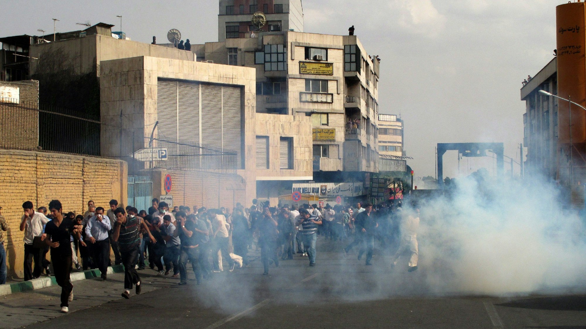 Menschen rennen in einer Straße in Teheran auf die Kamera zu. Sie fliehen vor einer Rauchwolke.