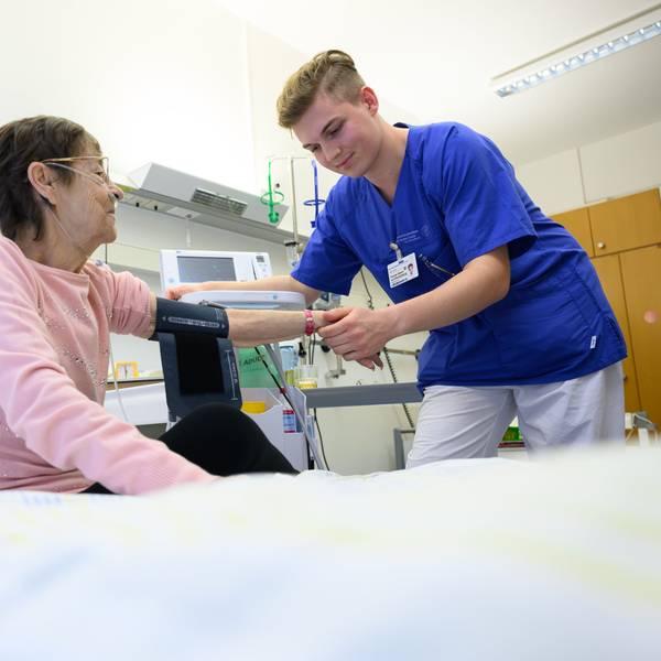 Ein junger Pflegefachmann legt auf der Station der Akutgeriatrie einer Patientin ein Blutdruckmessgerät um den Arm.