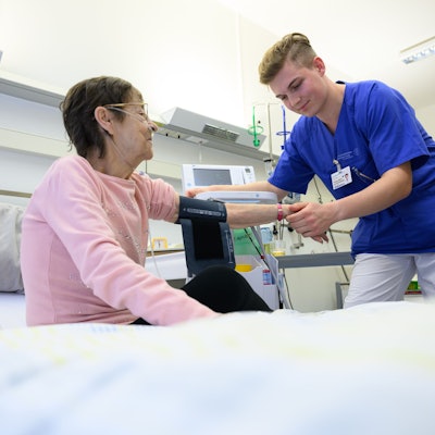 Ein junger Pflegefachmann legt auf der Station der Akutgeriatrie einer Patientin ein Blutdruckmessgerät um den Arm.