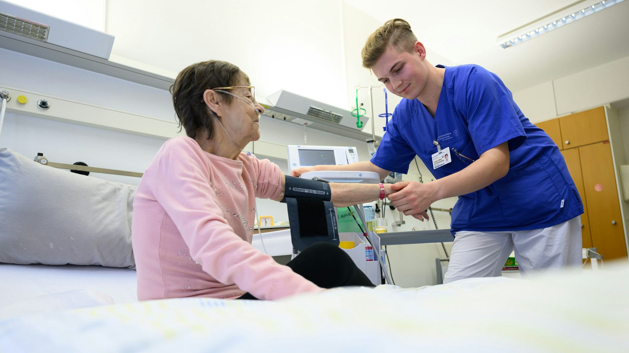 Ein junger Pflegefachmann legt auf der Station der Akutgeriatrie einer Patientin ein Blutdruckmessgerät um den Arm.