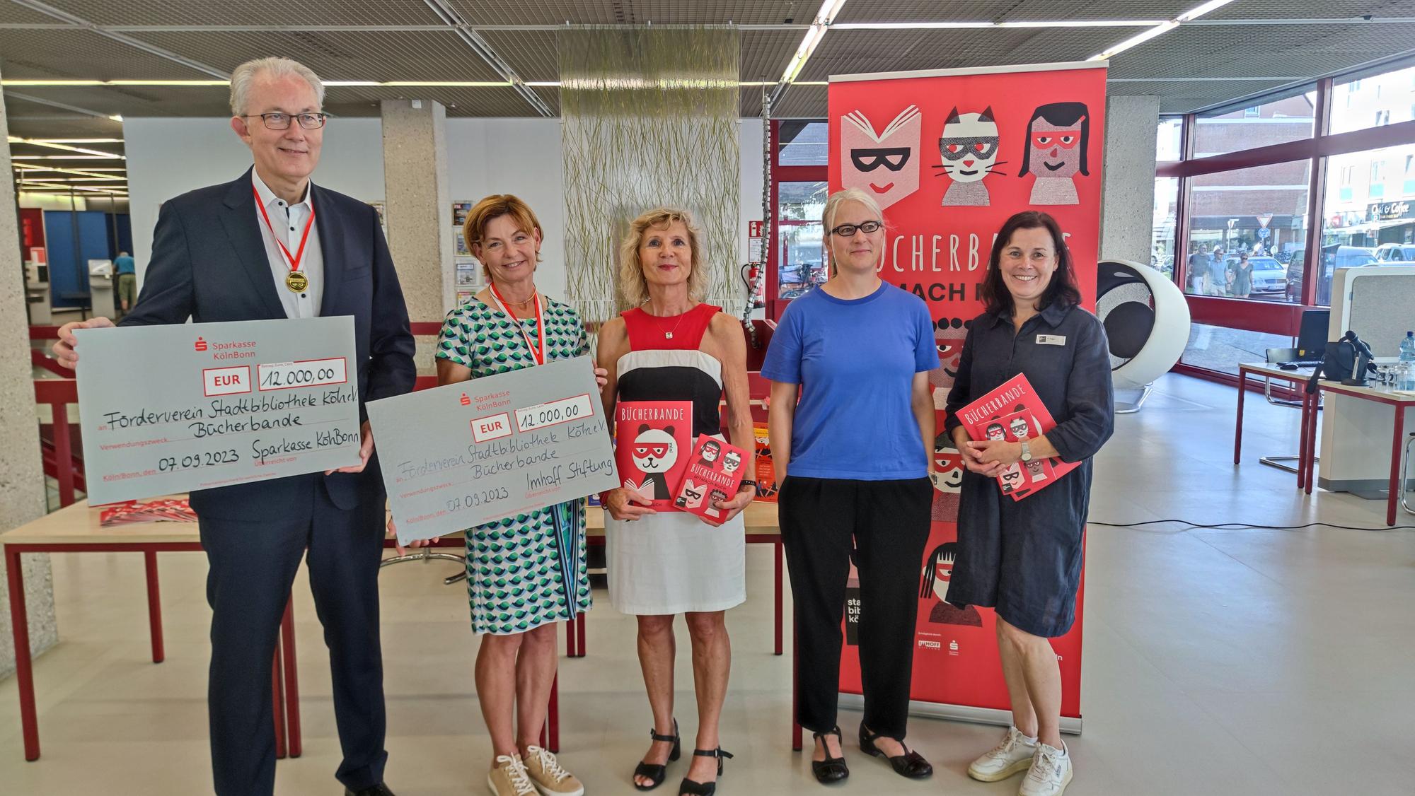 Gruppenfoto der fünf Personen. Voigt und Imhoff halten einen Scheck in der Hand, Vogt und Wigger halten die neuen Bücher in der Hand.