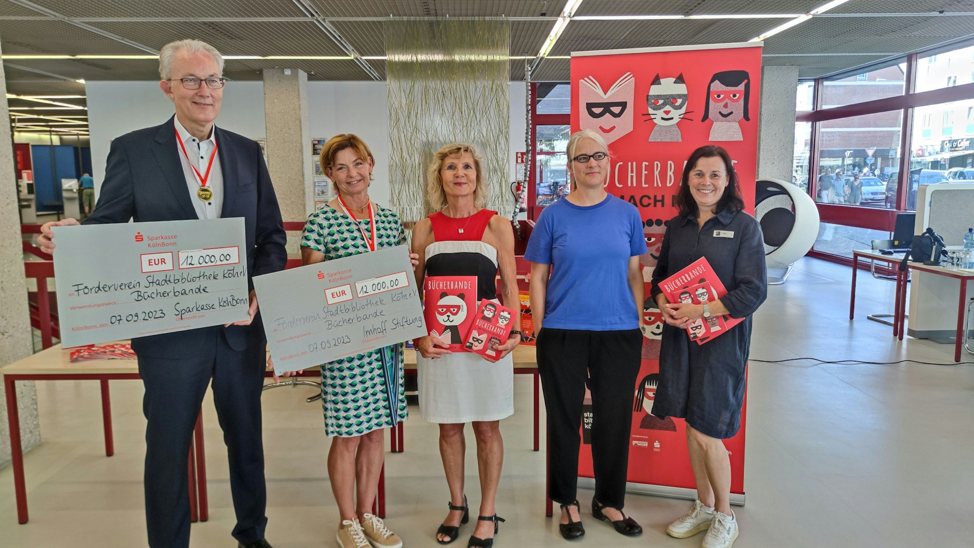 Gruppenfoto der fünf Personen. Voigt und Imhoff halten einen Scheck in der Hand, Vogt und Wigger halten die neuen Bücher in der Hand.