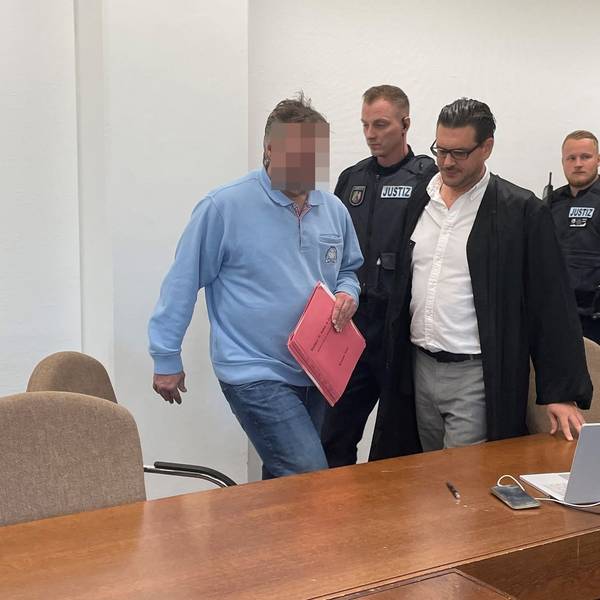Der Beschuldigte mit Verteidiger Hagen Schwindt und Wachtmeistern beim Prozessauftakt im Landgericht Köln.