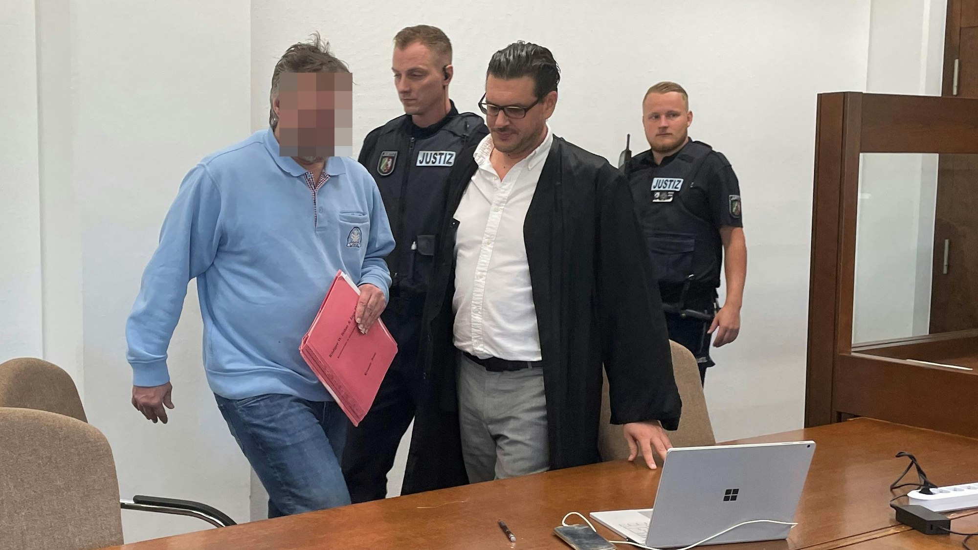 Der Beschuldigte mit Verteidiger Hagen Schwindt und Wachtmeistern beim Prozessauftakt im Landgericht Köln.