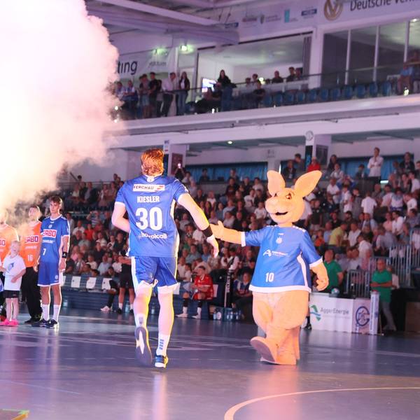 VfL-Handballer Tom Kiesler läuft in die Schwalbe-Arena und klatscht Maskottchen Gummi ab.