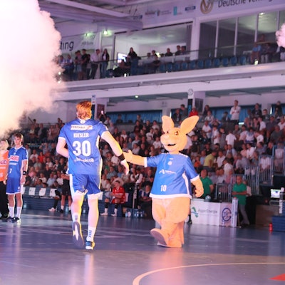 VfL-Handballer Tom Kiesler läuft in die Schwalbe-Arena und klatscht Maskottchen Gummi ab.