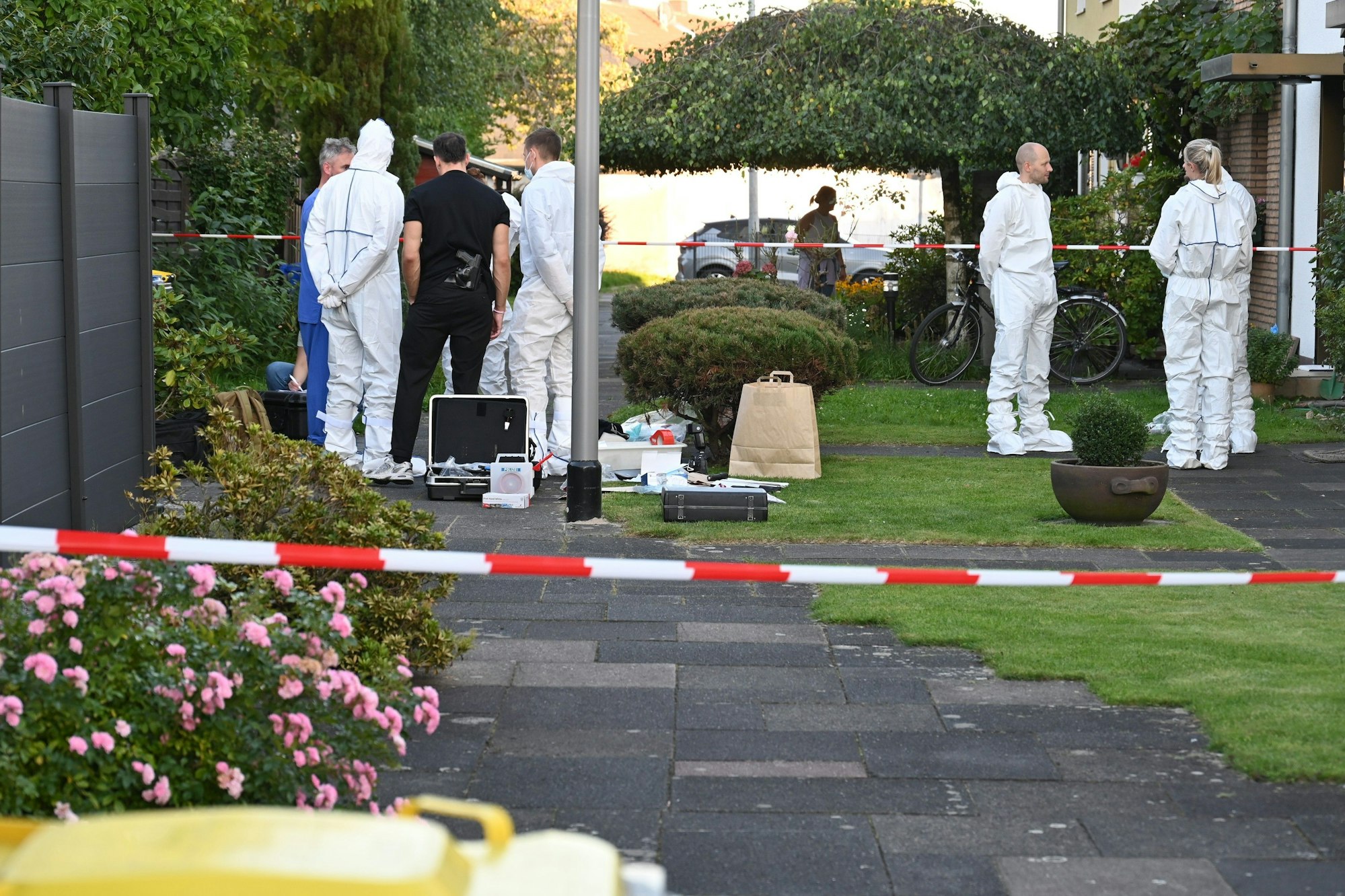 Das Bild zeigt mehrere Polizeibeamte in weißen Schutzanzügen vor dem Haus des Opfers.