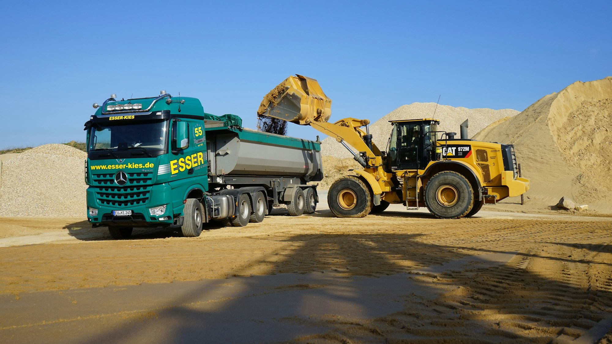 Ein Bagger lädt Sand auf einen Lkw.